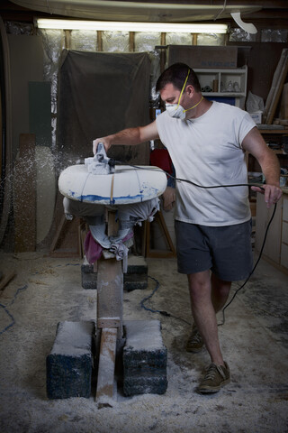 Mature man sanding a surfboard in his garage stock photo