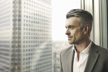 Portrait of mature businessman looking out of office window - CUF34587