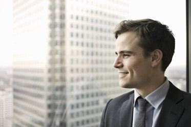 Portrait of young businessman looking out of office window - CUF34588