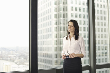 Porträt einer jungen Geschäftsfrau mit Blick aus dem Bürofenster - CUF34594