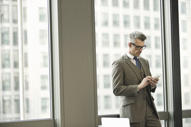 Businessman texting on smartphone in office - CUF34597