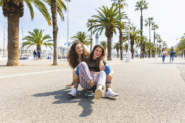 Carefree young woman and teenage girl having fun with a skateboard on a promenade with palms - WPEF00447