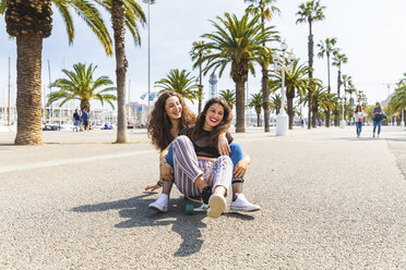 Unbeschwerte junge Frau und Teenager-Mädchen haben Spaß mit einem Skateboard auf einer Promenade mit Palmen - WPEF00447
