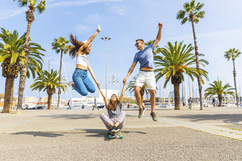 Unbekümmerte Freunde haben Spaß mit einem Skateboard auf einer Promenade mit Palmen - WPEF00451
