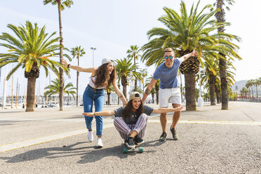 Unbekümmerte Freunde haben Spaß mit einem Skateboard auf einer Promenade mit Palmen - WPEF00452