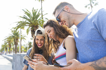 Glückliche Freunde teilen Handy auf einer Promenade mit Palmen - WPEF00454