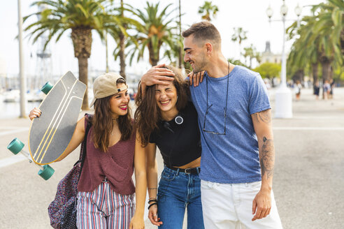 Glückliche Freunde mit einem Skateboard auf einer Promenade mit Palmen - WPEF00467