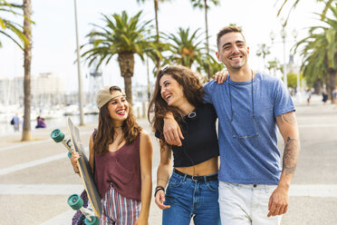 Happy friends with a skateboard walking on a promenade with palms - WPEF00468