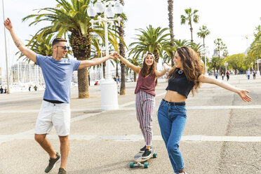 Unbekümmerte Freunde haben Spaß mit einem Skateboard auf einer Promenade mit Palmen - WPEF00470