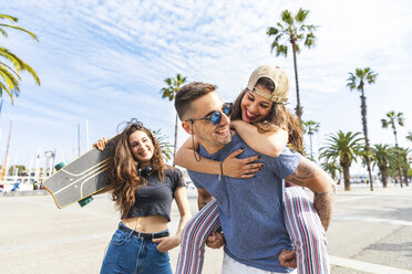 Glückliche Freunde mit einem Skateboard, die sich auf einer Promenade mit Palmen vergnügen - WPEF00472