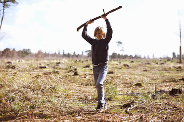 Boy holding up a stick in a plantation clearing - CUF34649