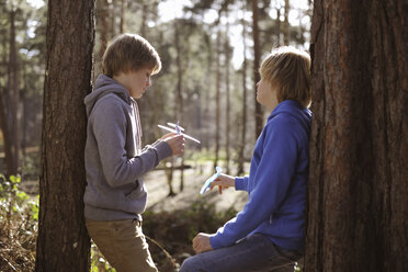 Twin brothers holding toy airplanes chatting in forest - CUF34661