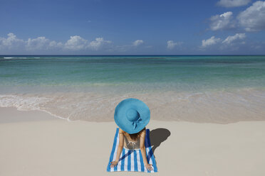 Junge Frau mit blauem Sonnenhut entspannt am Strand - CUF34666