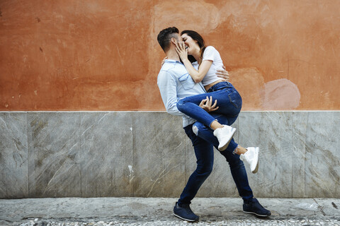 Carefree couple in love in front of a wall outdoors stock photo
