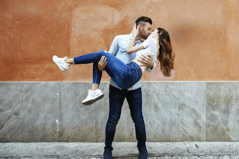 Unbeschwertes verliebtes Paar, das sich vor einer Mauer im Freien küsst, lizenzfreies Stockfoto