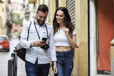 Lächelndes Touristenpaar mit Mobiltelefon beim Spaziergang in der Stadt - JSMF00312