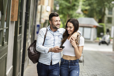 Lächelndes Touristenpaar mit Mobiltelefon beim Spaziergang in der Stadt - JSMF00314