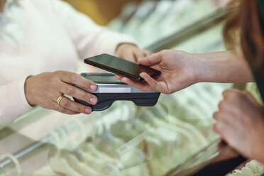 Close-up of woman paying with smartphone in a store - JSMF00335