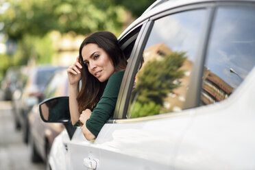 Young woman leaning out the window of her car in the city - JSMF00340