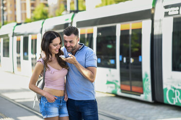 Ein Paar benutzt sein Smartphone, während es am Bahnhof auf die Straßenbahn wartet - JSMF00343