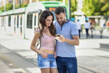 Couple looking at smartphone while waiting for tram at the station - JSMF00344