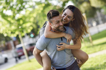 Happy man giving girlfriend a piggyback ride in park - JSMF00349