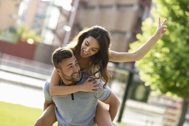 Happy man giving girlfriend a piggyback ride in park - JSMF00350