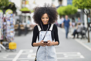 Smiling young woman with earphones looking at cell phone - JSMF00358