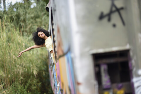 Glückliche junge Frau lehnt sich aus einem verlassenen und zerstörten alten Zug, lizenzfreies Stockfoto