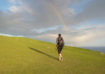 Young female hiker, hiking up hill toward rainbow - CUF34727