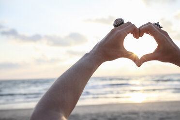 Female hands making heart shape at sunset on beach - CUF34765