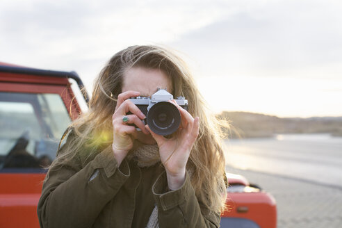 Mittlere erwachsene Frau beim Fotografieren mit Spiegelreflexkamera auf einem Parkplatz an der Küste - CUF34808