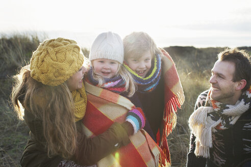 Mid adult couple in sand dunes with their son and daughter wrapped in blanket - CUF34811