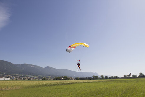 Fallschirmspringerin, die mit dem Fallschirm über einem Feld abspringt und sich der Landezone nähert, Grenchen, Bern, Schweiz - CUF34819