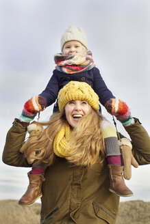 Lächelnde erwachsene Frau, die ihre Tochter an der Küste auf den Schultern trägt - CUF34828