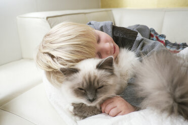 Cute three year old boy with eyes closed hugging cat on sofa - CUF34833