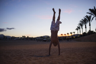 Silhouettierter Junge macht Handstand am Strand in der Abenddämmerung - CUF34861