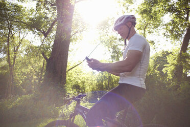 Radfahrer benutzt Smartphone im Wald - CUF34867