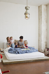 Familie mit drei Töchtern, die im Bett Bücher lesen - CUF34911
