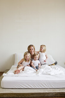 Porträt einer mittelalten Frau im Bett mit drei Töchtern - CUF34912