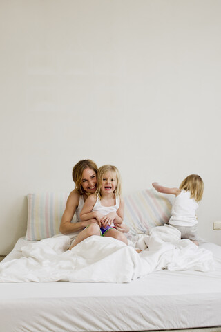 Porträt einer mittleren erwachsenen Frau mit zwei Töchtern im Bett sitzend, lizenzfreies Stockfoto
