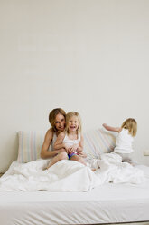 Porträt einer mittleren erwachsenen Frau mit zwei Töchtern im Bett sitzend - CUF35031