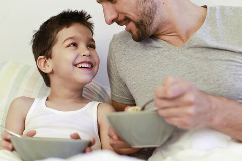 Vater und kleiner Sohn beim Frühstück im Bett, lizenzfreies Stockfoto