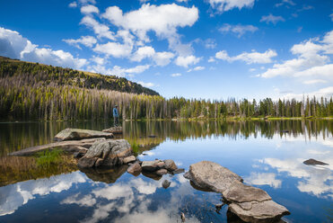 Hiker on pathway of rocks, surrounded by reflections of clouds, on Quinescoe Lake, Cathedral Lakes Provincial Park, British Columbia, Canada - CUF35098