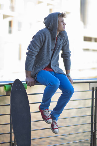 Junger Mann, der von einem Geländer am Flussufer blickt, lizenzfreies Stockfoto