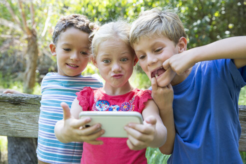 Drei Kinder im Garten machen ein Selfie mit ihrem Smartphone - CUF35256