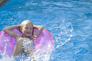 Girl lying on her back on inflatable ring in garden swimming pool - CUF35265