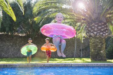 Mädchen springt mit aufblasbarem Ring in den Swimmingpool im Garten - CUF35267