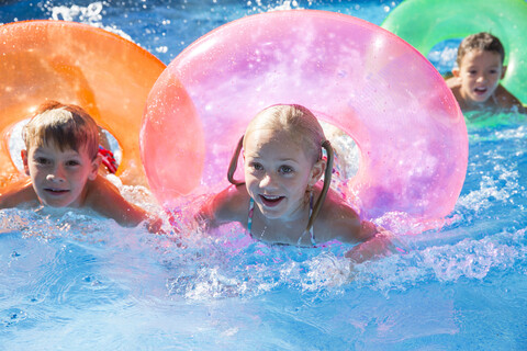 Drei Kinder schwimmen mit aufblasbaren Ringen im Gartenschwimmbad, lizenzfreies Stockfoto