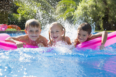 Portrait of three children splashing on inflatable mattress in garden swimming pool - CUF35273